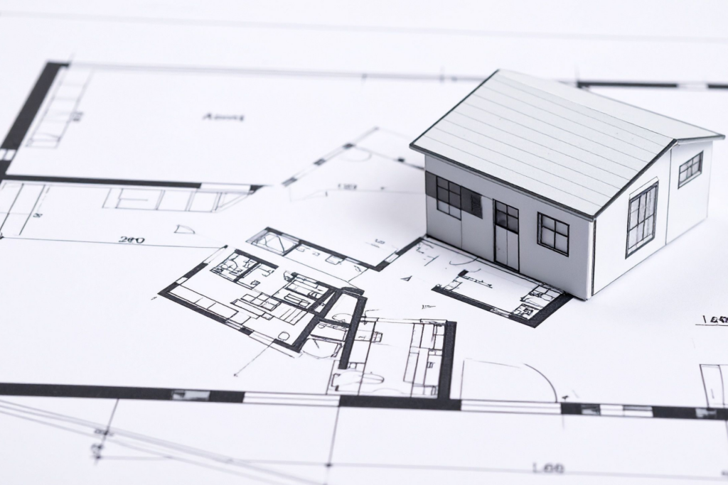 Paper model house sitting on architectural blueprints illustrating HOA architectural control committee review in Michigan