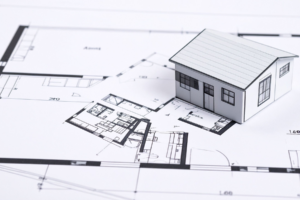 Paper model house sitting on architectural blueprints illustrating HOA architectural control committee review in Michigan